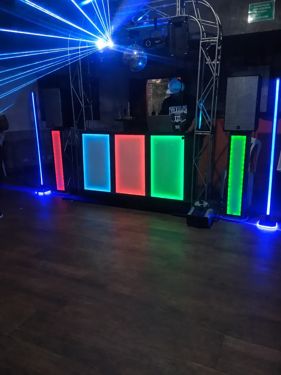Estrutura noturna com laser e LED. Cabine iluminada em vermelho, azul e verde, com feixes de laser e globo espelhado.