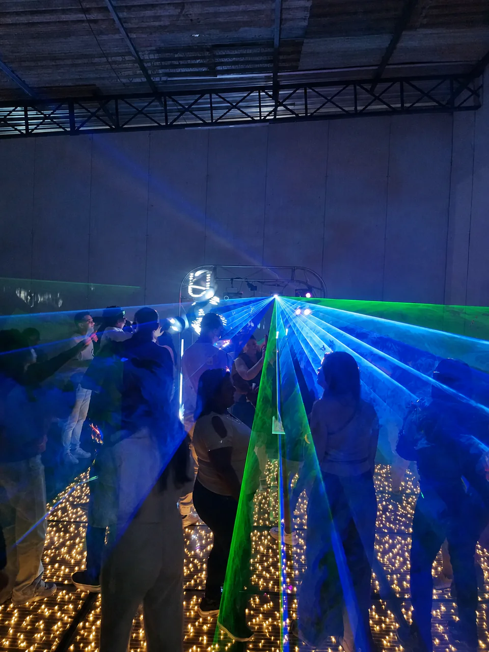 Convidados dançando sobre pista de LED com feixes de luz azul e verde.