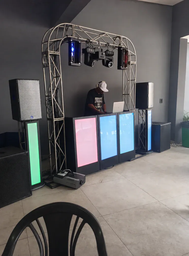 Estrutura de DJ em ambiente contemporâneo. Treliça curva, caixas de som e cabine iluminada compondo um cenário limpo antes da chegada do público.