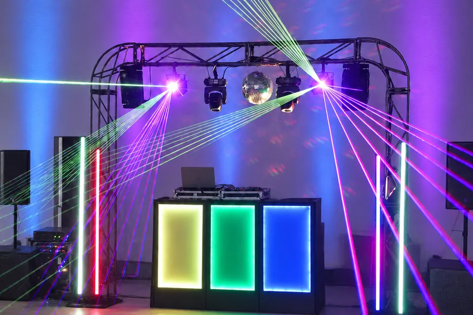 Cabine de DJ iluminada com lasers verdes, azuis e rosa na comemoração de formatura.