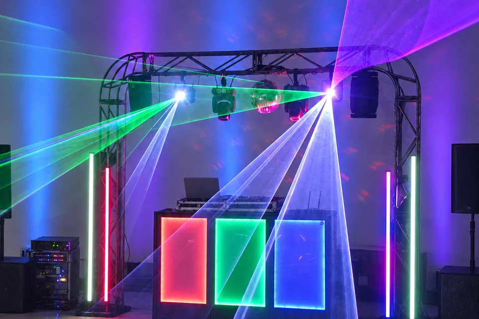 Iluminação cênica azul e violeta com lasers sobre a estrutura do DJ na festa de formatura.